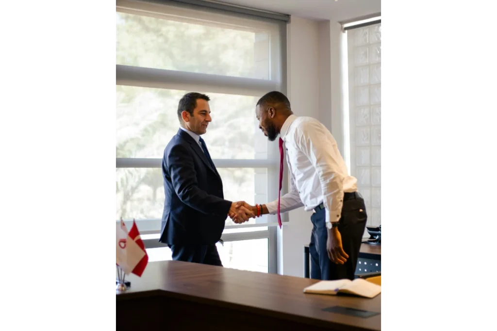 Two business professionals shaking hands in a brightly lit, modern office setting.